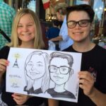 Two smiling teenagers hold up Caricatures at Bastille Day in Healdsburg during an outdoor event.