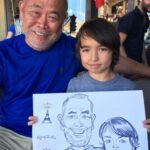 An older man and a boy pose with a caricature drawing at a Caricatures Bastille Day event in Healdsburg.