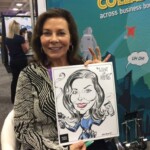Woman seated at an event holding a black and white caricature drawing of herself.