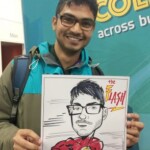 A man smiles and holds a caricature of himself dressed as The Flash superhero at an event booth.
