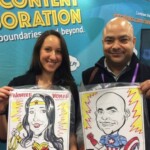 Two people smiling and holding caricature portraits of themselves as Wonder Woman and Captain America at an event.
