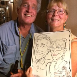 Two smiling people pose together holding a caricature drawing of themselves at an event.