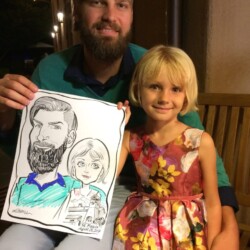 A man and a young girl sit on a bench holding a caricature drawing of themselves.