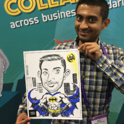 A man holds a caricature of himself as Batman in front of a colorful conference backdrop.