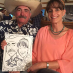 A man in a cowboy hat and a woman hold a caricature drawing of themselves while sitting together indoors.