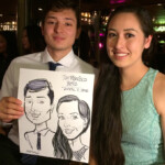 A man and woman sit together indoors, holding a caricature portrait of themselves dated April 7, 2016.