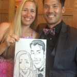 A smiling couple poses indoors, holding a caricature portrait of themselves.
