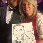 A smiling man and woman in formal attire hold a caricature drawing of themselves at an event.