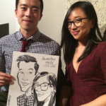 Two people sit together, one holding a black-and-white caricature portrait of themselves.