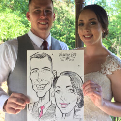 A bride and groom in wedding attire hold a caricature drawing of themselves under an outdoor gazebo.