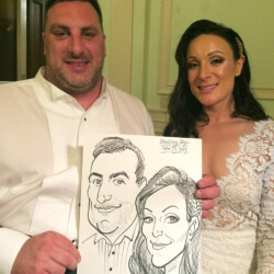 A man and woman in formal attire hold a caricature drawing of themselves at an event.