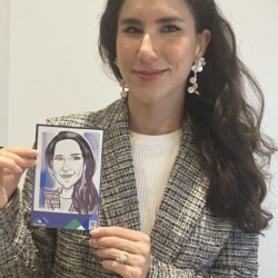 Woman in a plaid blazer holds up a black-and-white caricature drawing of herself against a plain background.