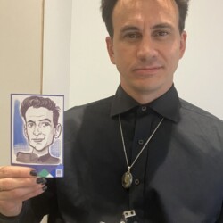 Man in a black shirt holding a black-and-white caricature of himself, wearing a conference badge around his neck.